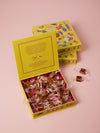 Yellow box of chocolates with floral design on a pink background